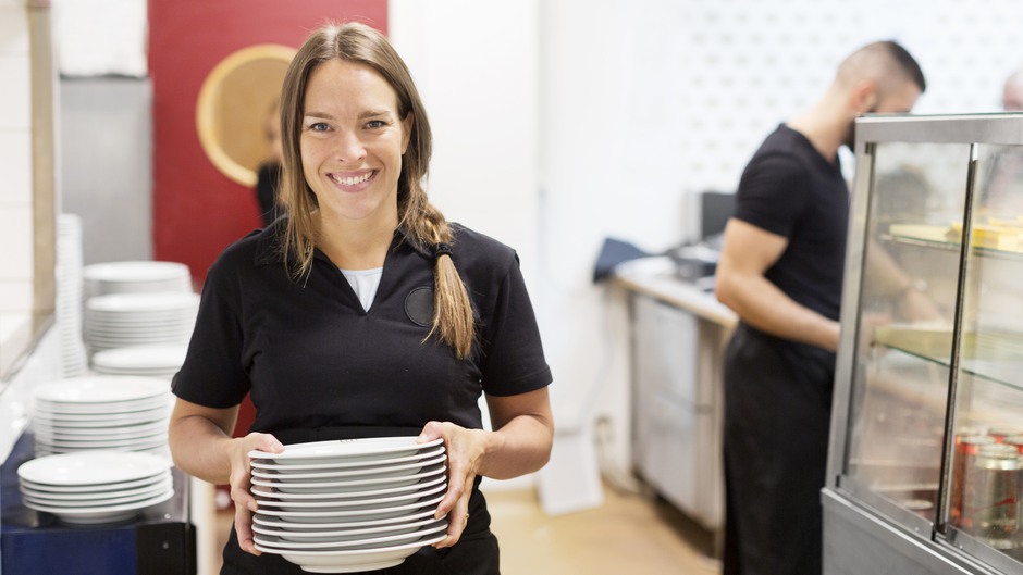 Servitris bär tallrikar i restaurangkök.